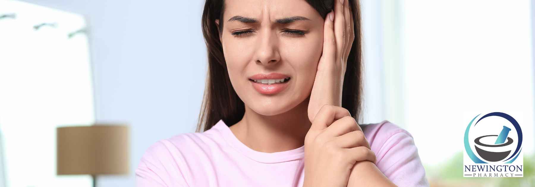 woman in pink shirt clutching ear in discomfort