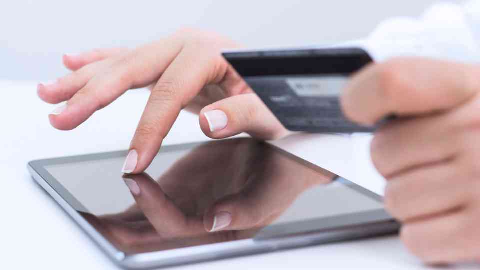 person scrolling on tablet holding credit card