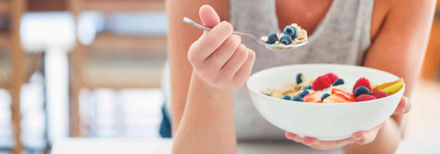 woman eating berries from bowl with spoon