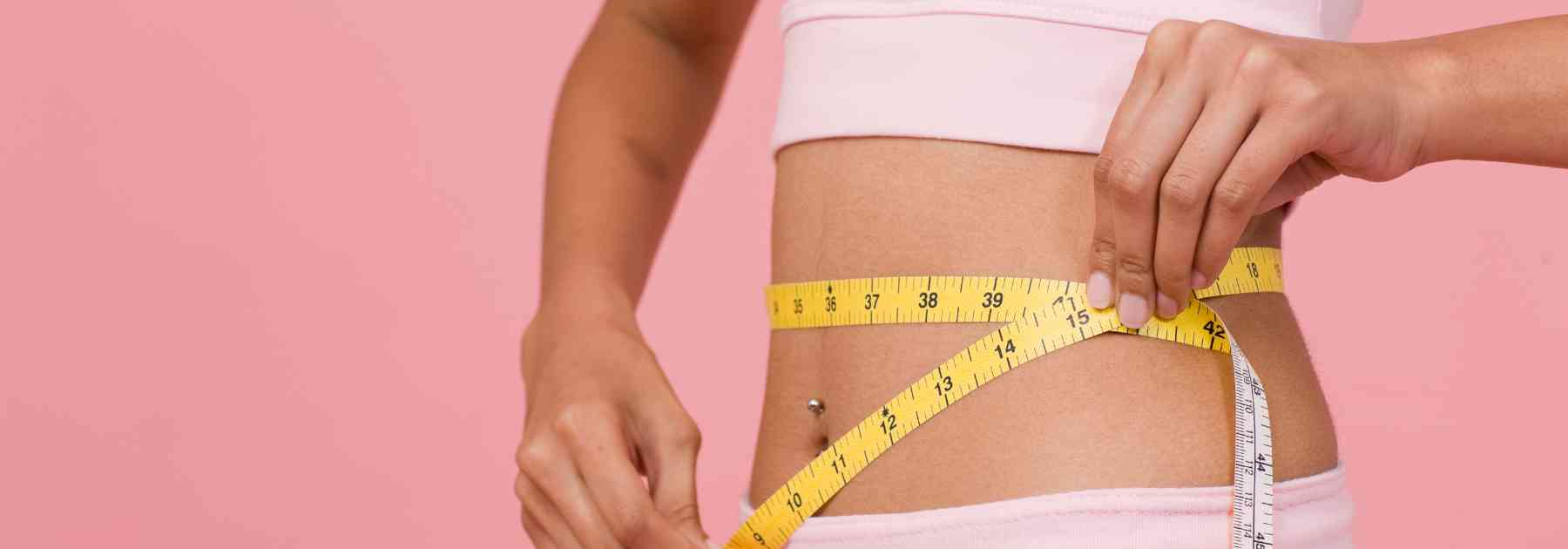 woman measuring her waist against pink background
