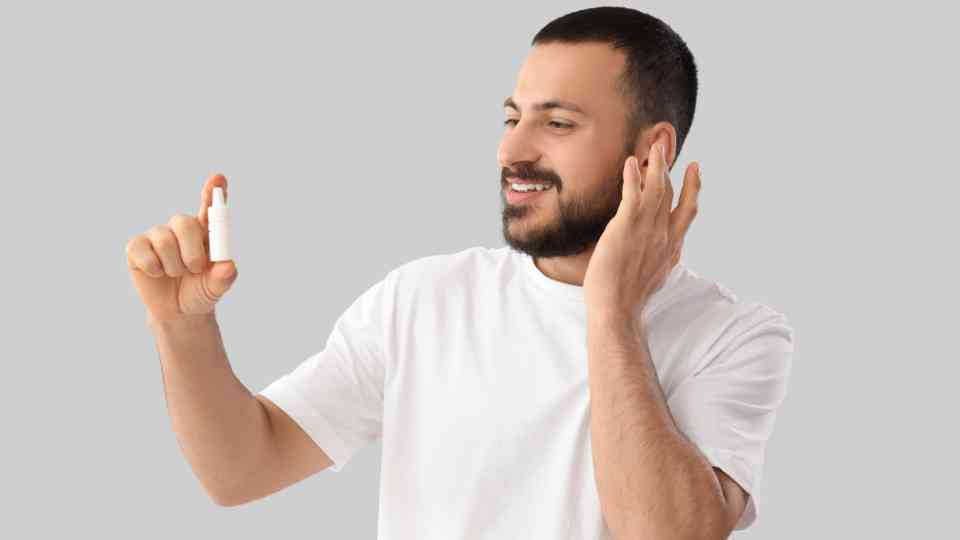 man holding ear and bottle of ear drops smiling