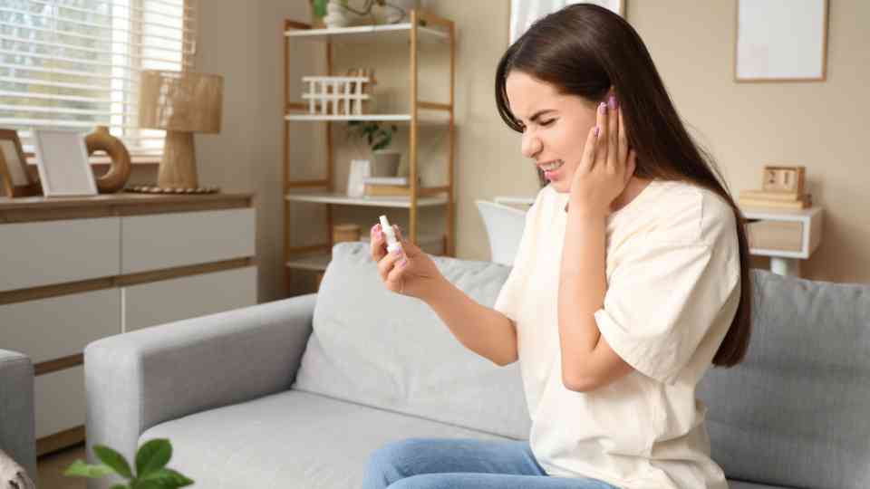 young woman holding her ear and bottle of ear wax drops