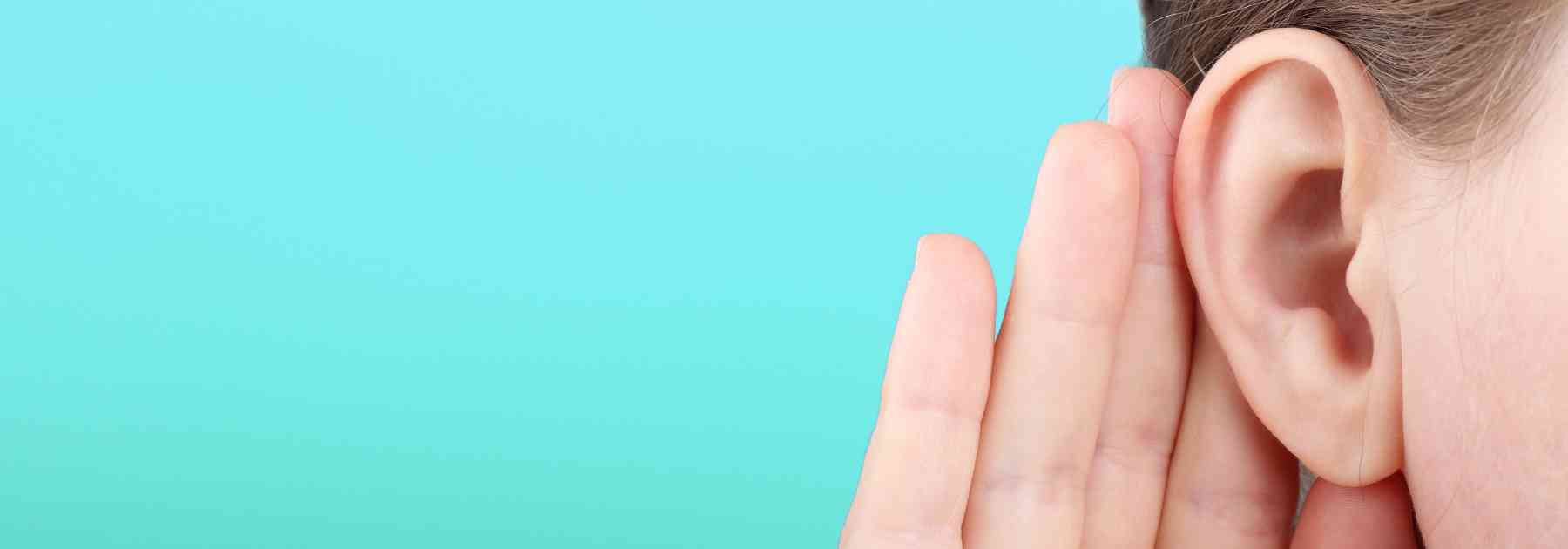 person holding their ear on turquoise background