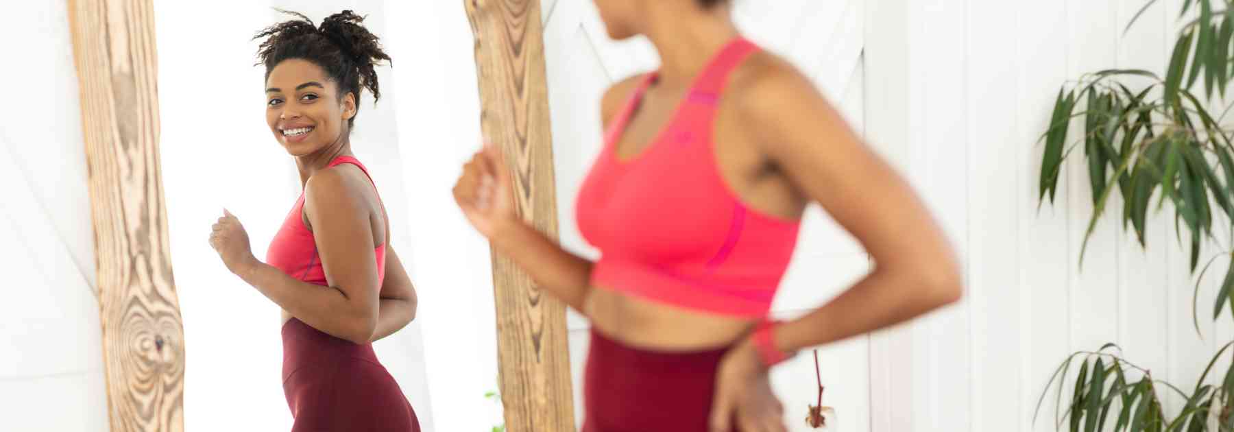 young woman in workout gear smiling and looking in mirror
