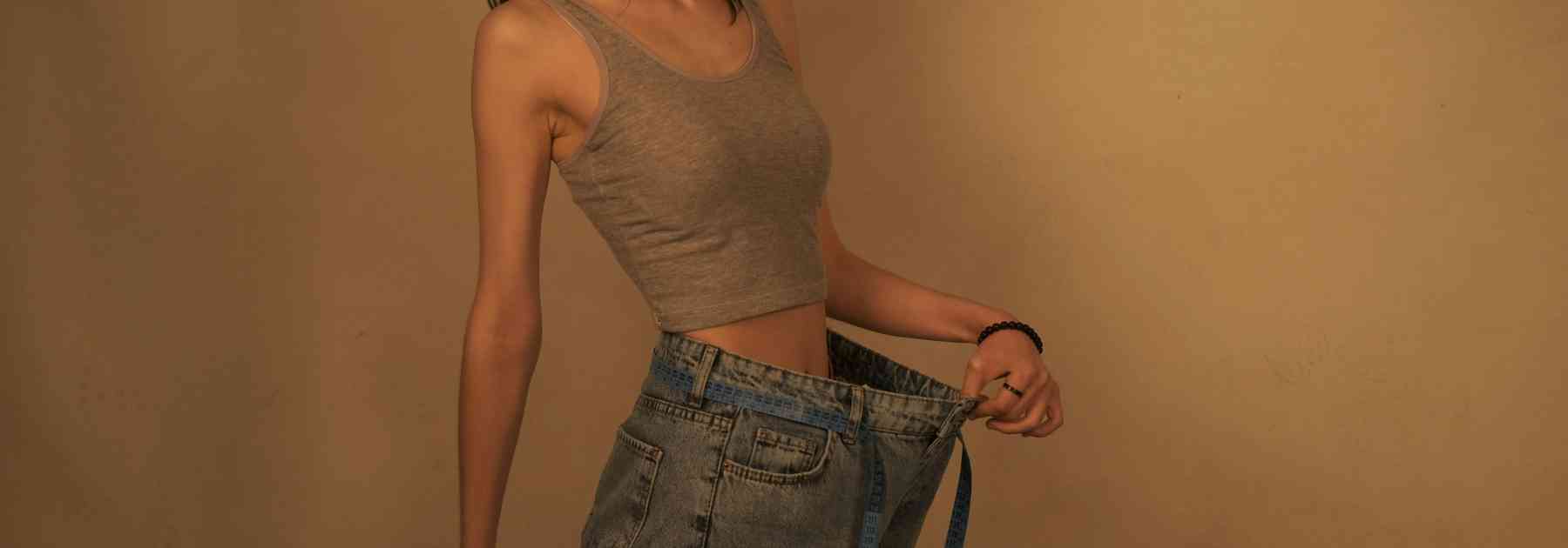 woman wearing jeans too big on orange background