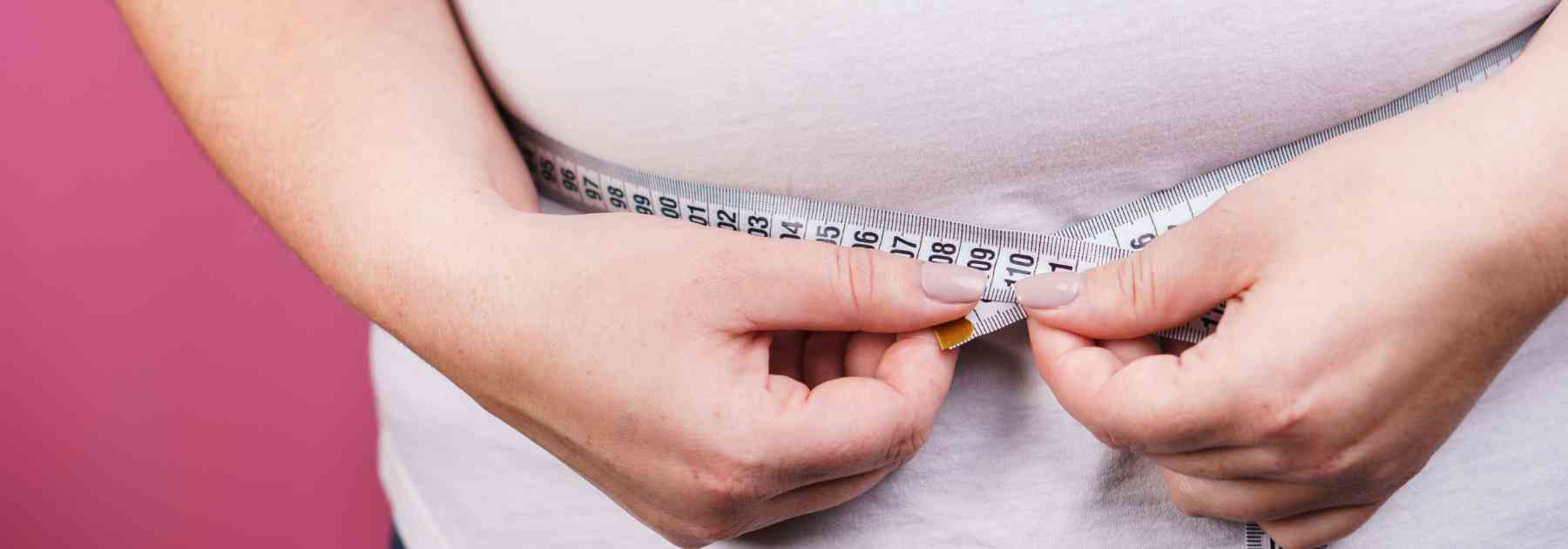 overweight woman measuring waist on pink background