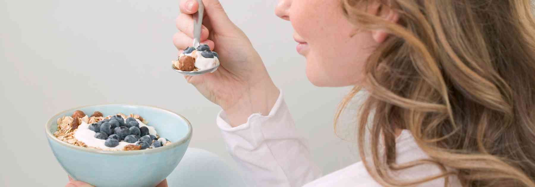 woman eating berries from bowl with spoon