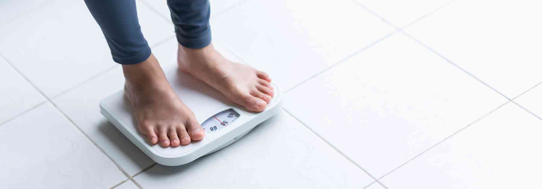 person in grey workout gear and bare feet standing on scales