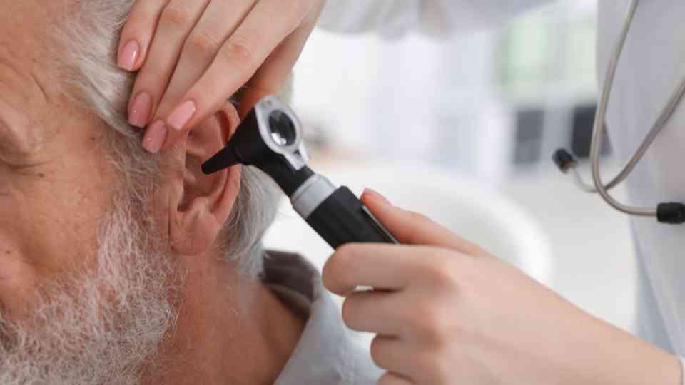 doctor examining ear of older male patient