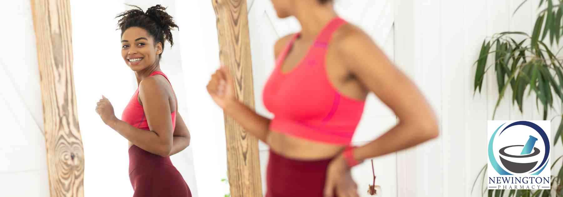 young woman in workout gear smiling and looking in mirror
