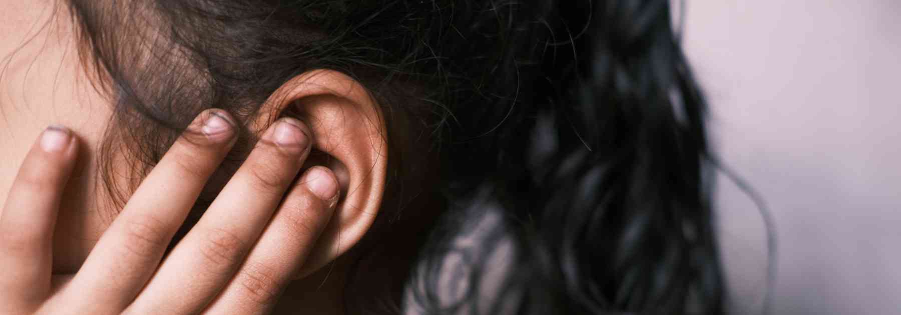 woman with dark hair clutching ear in discomfort
