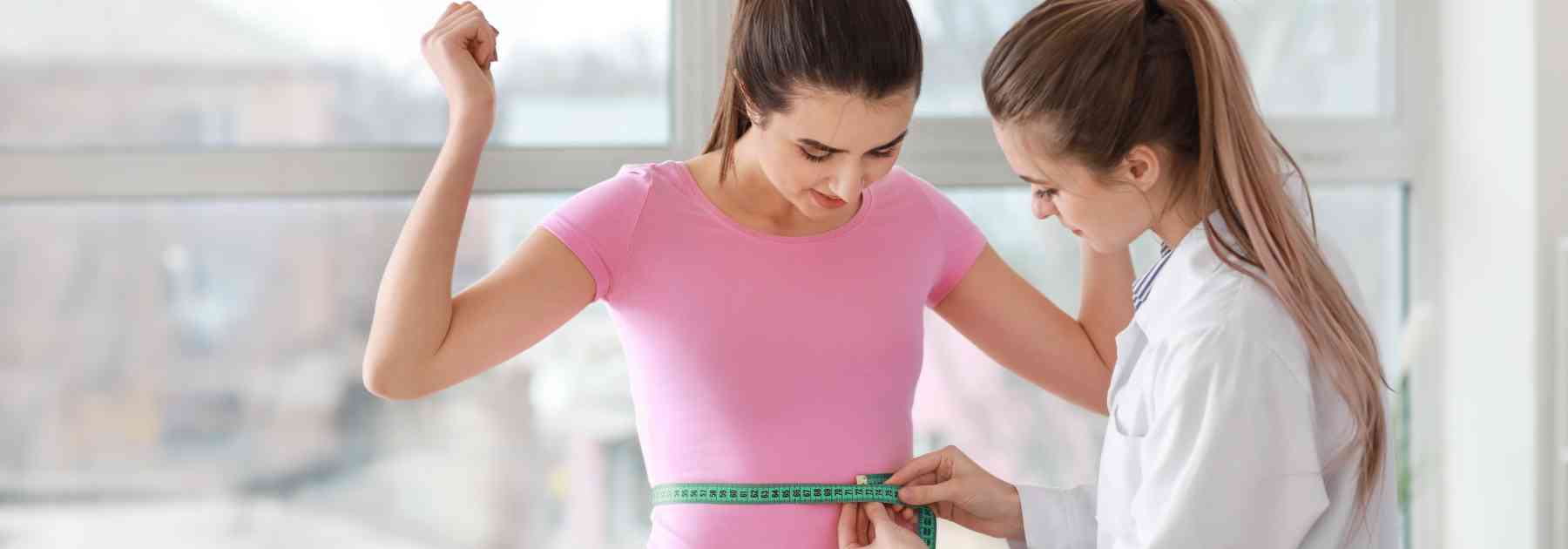female doctor measuring waist of female patient in pink shirt