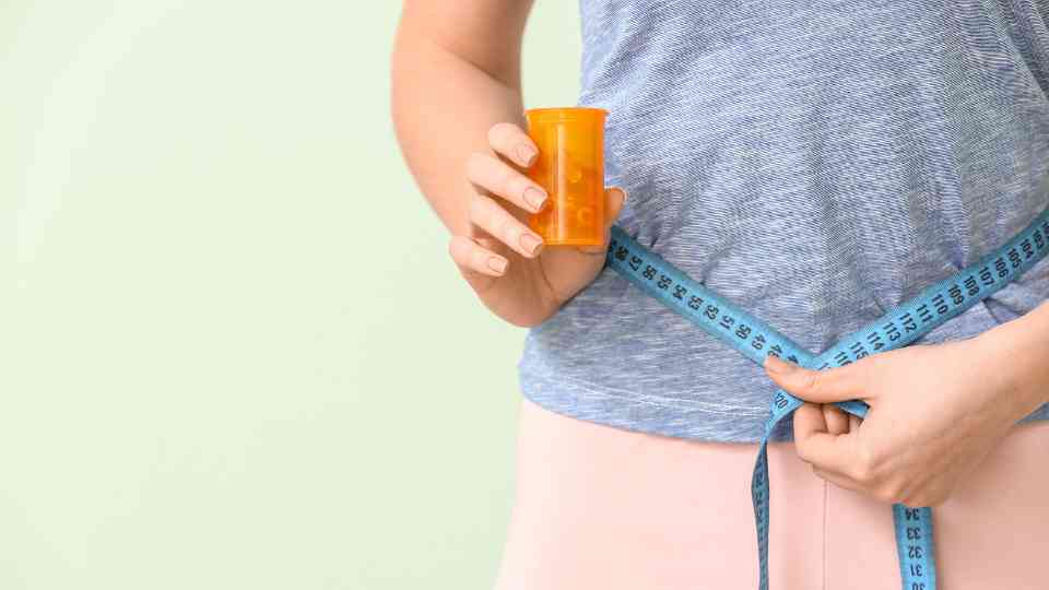 person measuring their waist holding weight loss supplements