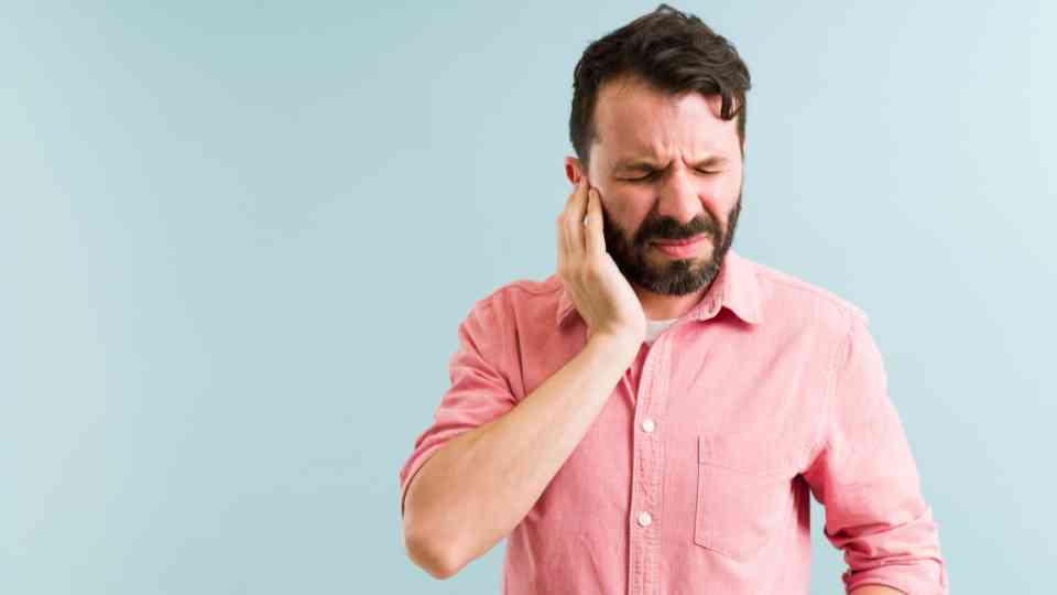 man holding his ear in discomfort on green background