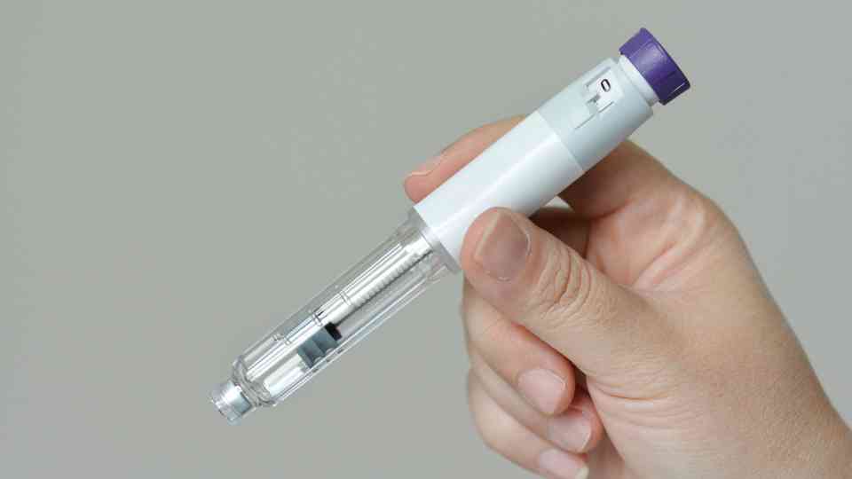 person holding weight loss injection on grey background