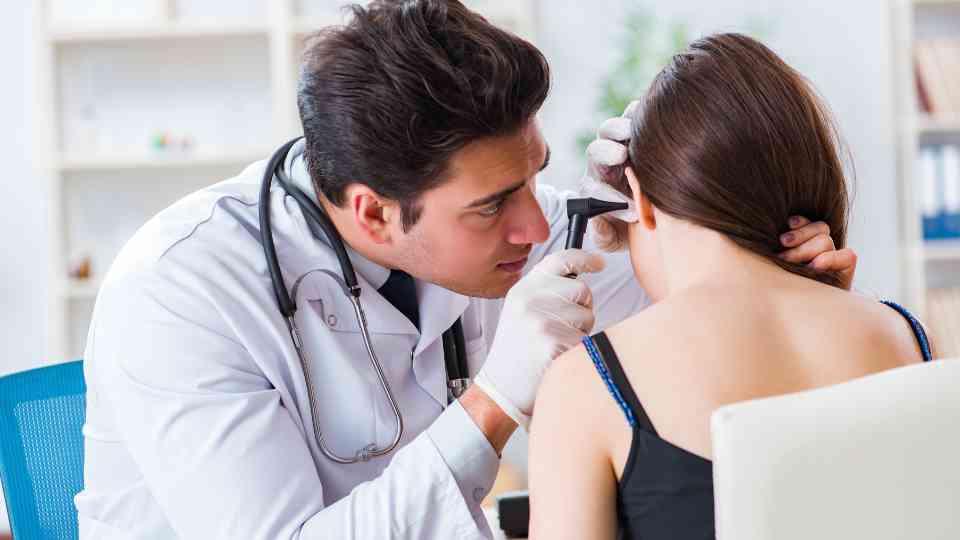 male doctor examining ear of female patient