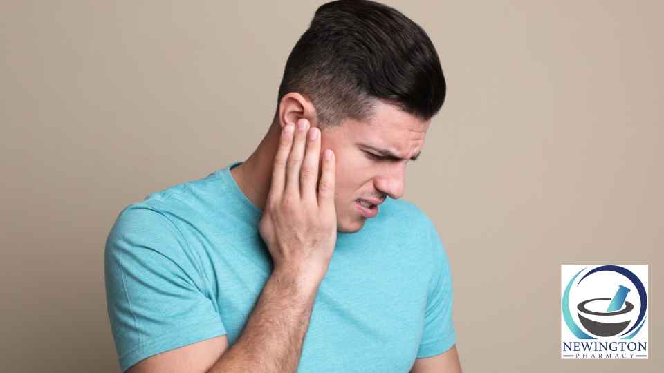 young man in blue t-shirt clutching ear in discomfort
