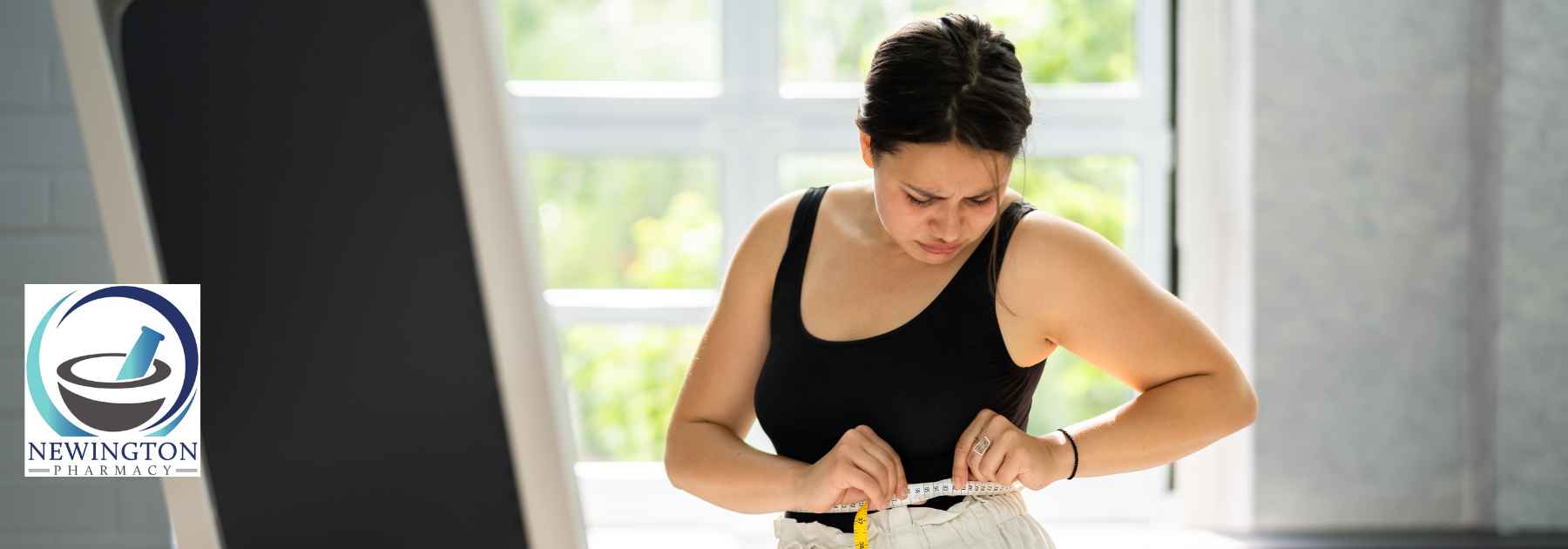 woman in workout gear measuring waist in front of mirror